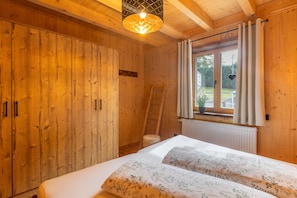 A wooden room with a bed, a wardrobe, a window with curtains, and a ladder.