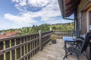 A wooden deck with a table and chairs, overlooking a green landscape with houses.