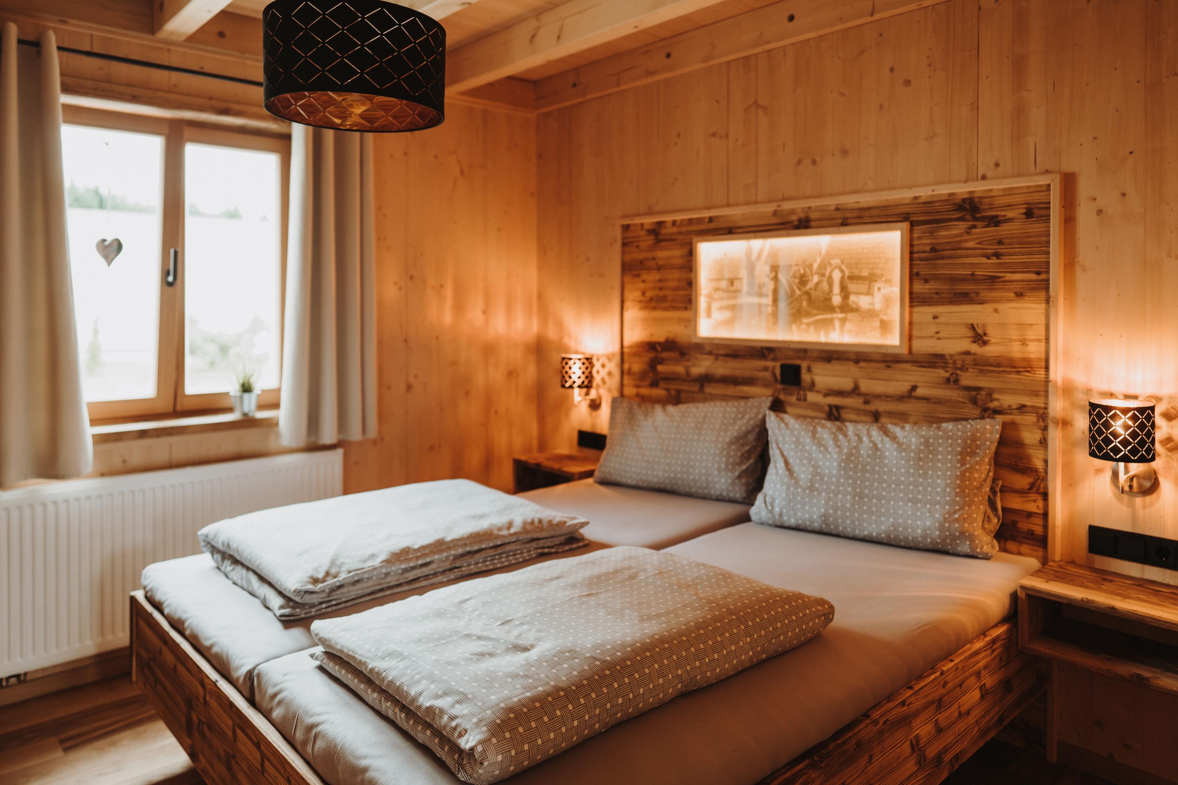 Une pièce en bois avec un lit, deux tables de chevet, une fenêtre et un tableau accroché au mur.