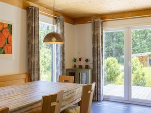 A dining area with a wooden table and chairs, a hanging light fixture, and a view through a glass door to an outdoor deck. - Cabin in Annaberg With Swimming Pool (Annaberg-Lungoetz)