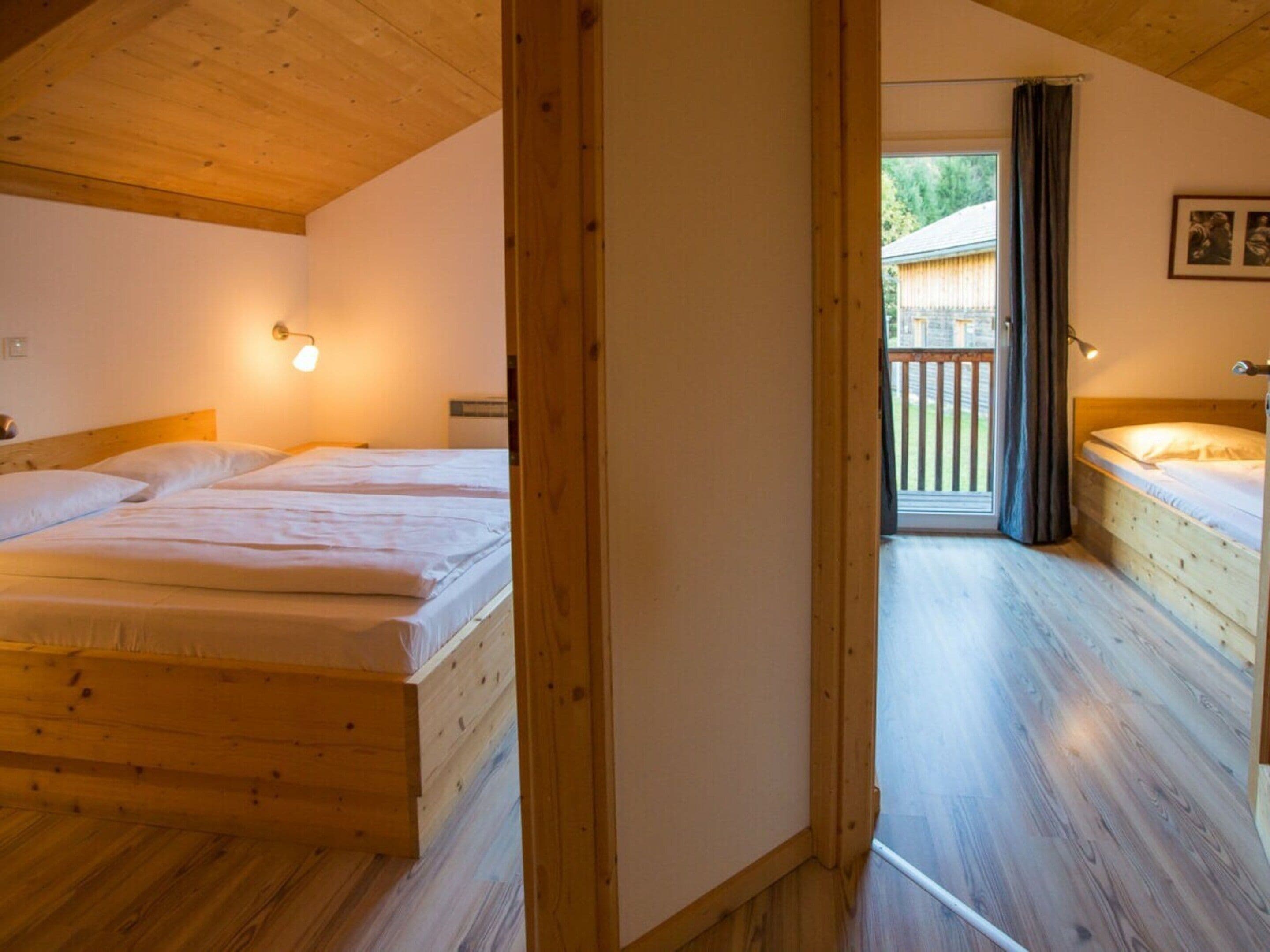 A room with two wooden beds, a wooden ceiling, and a view of a balcony.
