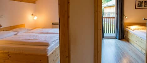 A room with two wooden beds, a wooden ceiling, and a view of a balcony.