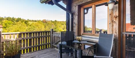 A wooden deck with a table and chairs, overlooking a forested area.