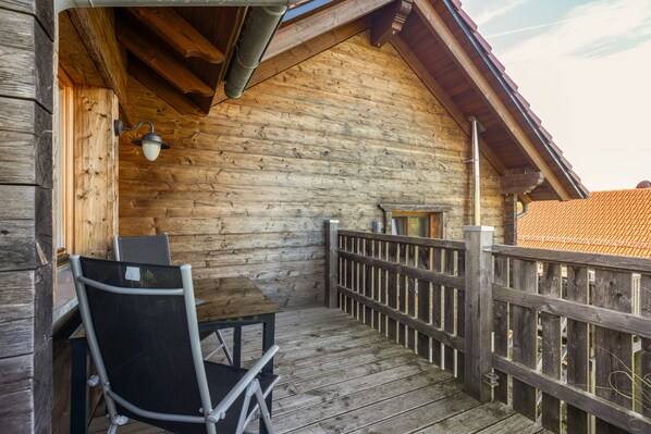 En træterrasse med et bord og stole, et gelænder og udsigt til et rødt tegltag.