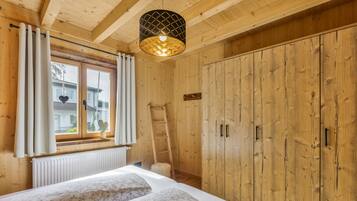 Een slaapkamer met houten vloer, een bed, een raam met gordijnen, een radiator en een kledingkast.