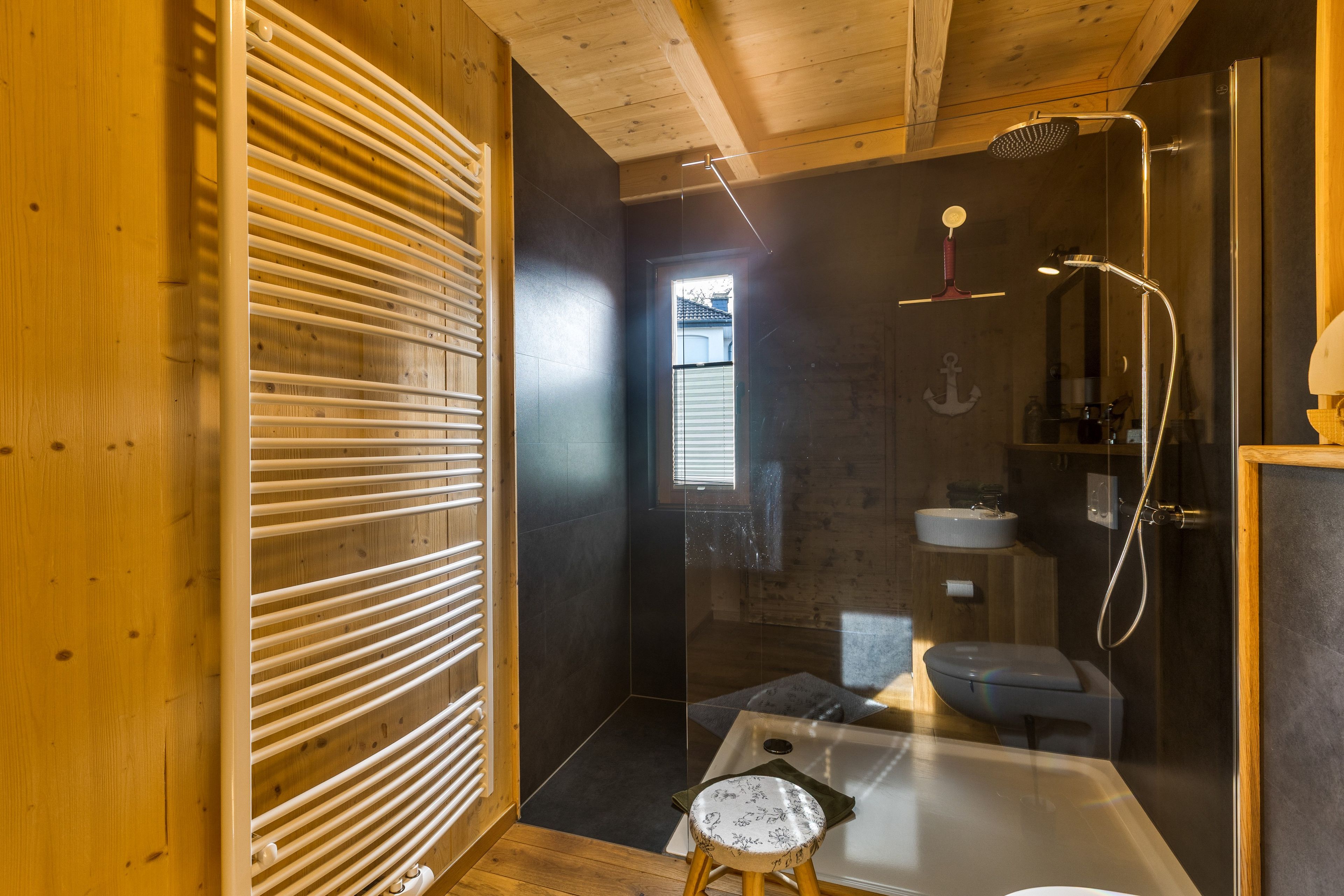 A modern bathroom with a wooden interior, a glass shower enclosure, and a small stool.