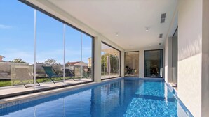 Ein moderner, überdachter Pool mit Glaswänden, Fliesenboden und Blick ins Freie.