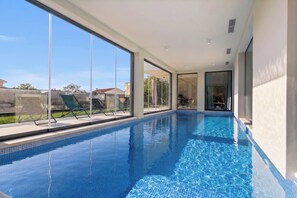 A modern indoor swimming pool with clear glass walls, a tiled floor, and a view of the outside. - Villa Oliva Mare with heated pool (Bale)