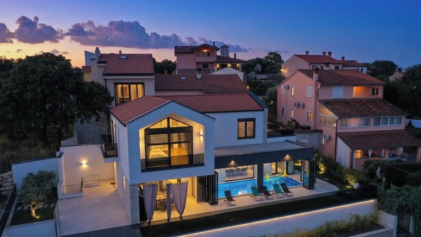 Ein modernes, zweistöckiges Haus mit Swimmingpool, großen Fenstern und einer gut beleuchteten Fassade.