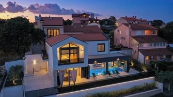 A modern two-story house with a swimming pool, large windows, and a well-lit exterior.