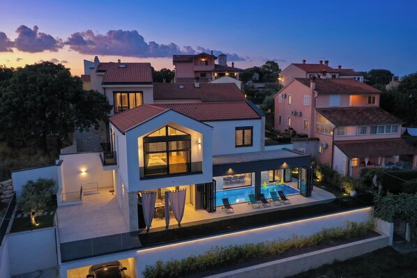 A modern two-story house with a swimming pool, large windows, and a well-lit exterior. - Villa Oliva Mare with heated pool (Bale)