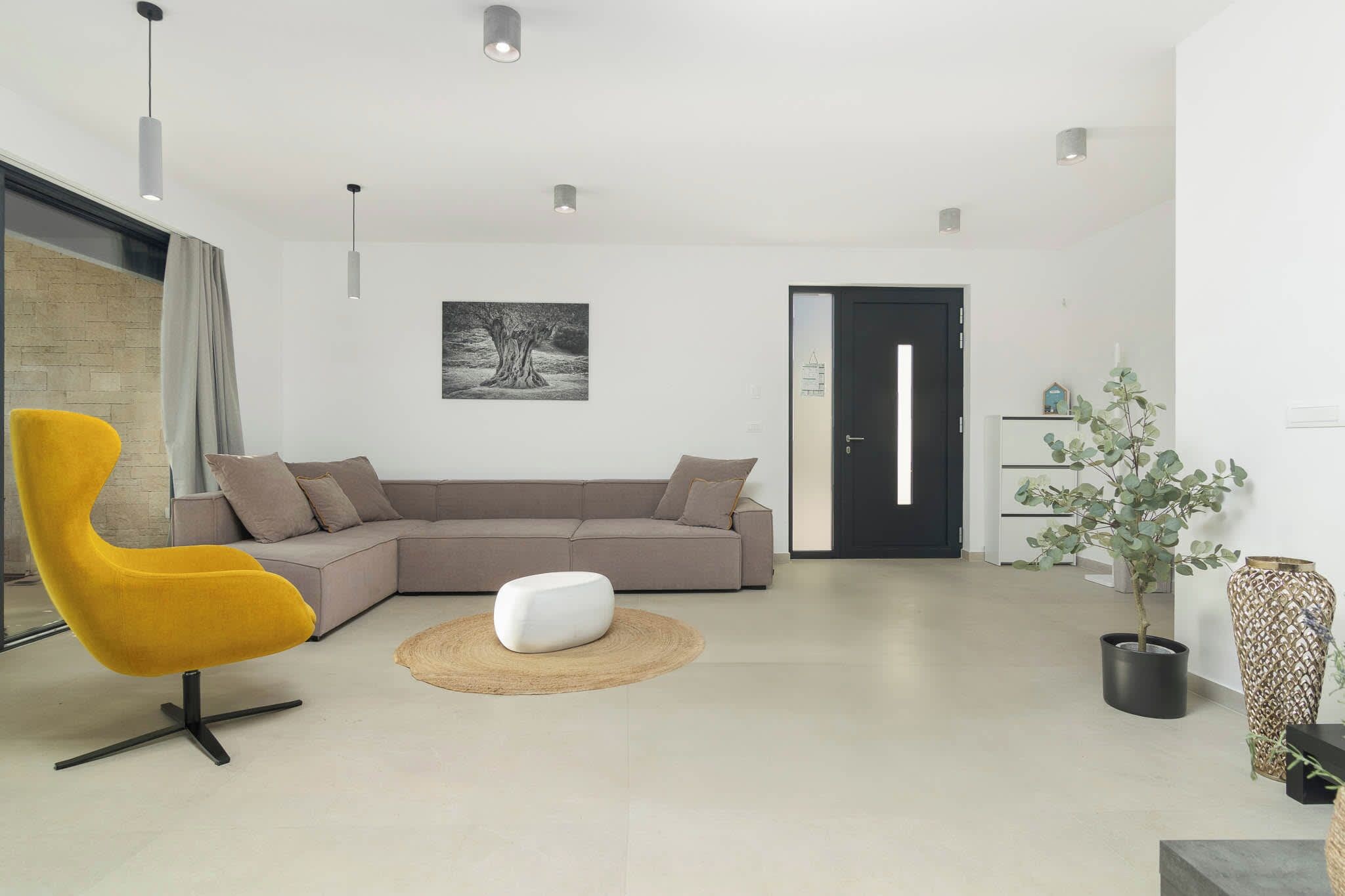 Ein modernes Wohnzimmer mit einem Ecksofa, einem gelben Sessel, einem weißen Hocker und einem Blumentopf.
