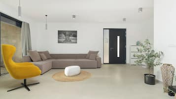 Ein modernes Wohnzimmer mit einem Ecksofa, einem gelben Sessel, einem weißen Hocker und einem Blumentopf.