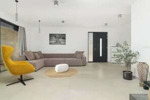 Un salon moderne avec un canapé d’angle, un fauteuil jaune, un pouf blanc et une plante en pot.