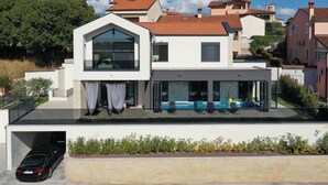 Ein modernes, zweistöckiges Haus mit flachem Dach, großen Fenstern und einer überdachten Sitzgelegenheit im Freien.