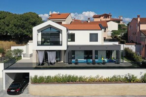 A modern two-story house with a flat roof, large windows, and a covered outdoor seating area. - Villa Oliva Mare with heated pool (Bale)