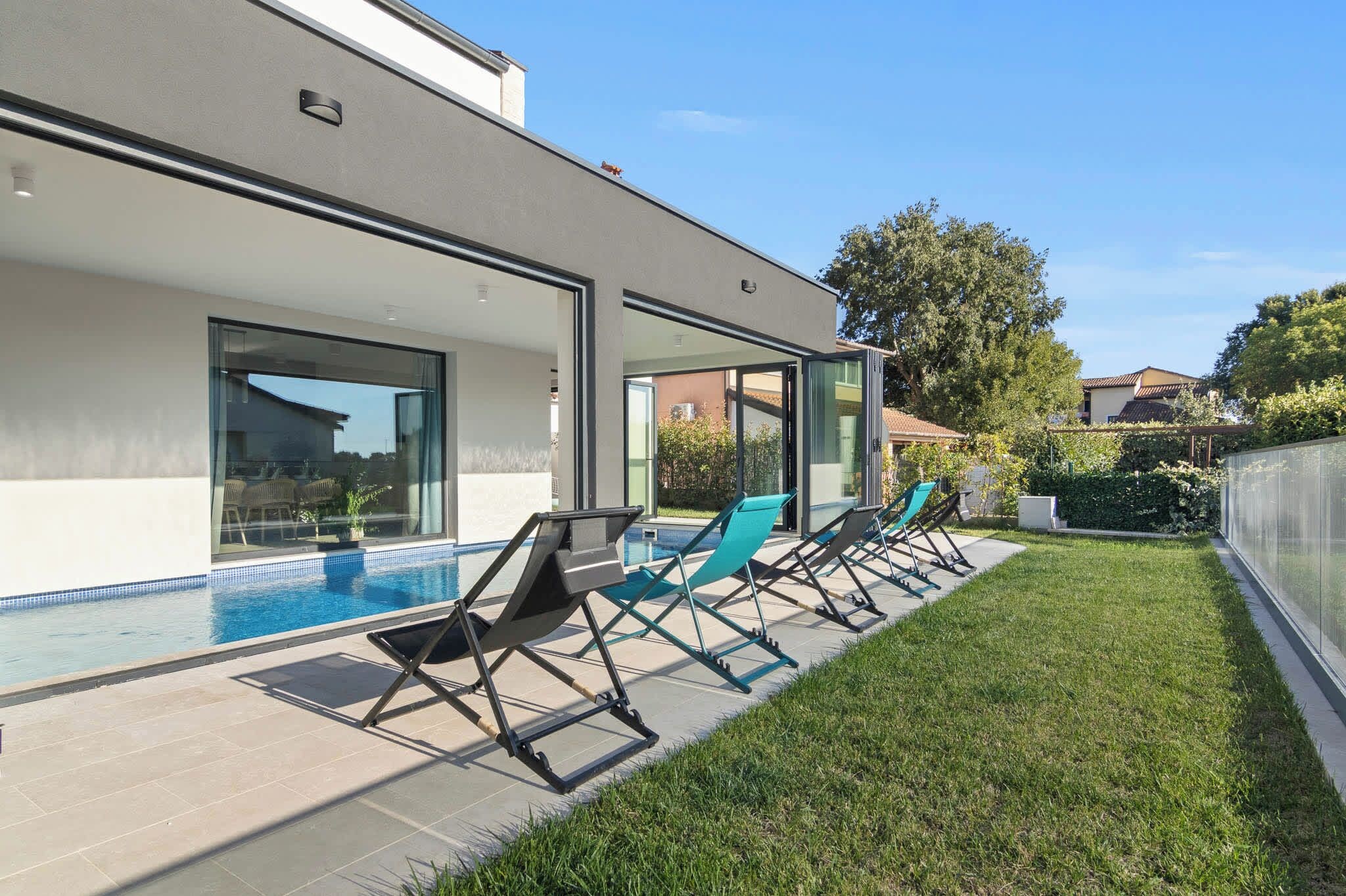Ein modernes Haus mit Schwimmbad, Sitzgelegenheiten im Freien und einem gepflegten Rasen.