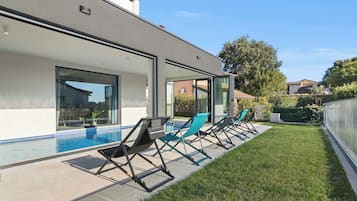 Ein modernes Haus mit Schwimmbad, Sitzgelegenheiten im Freien und einem gepflegten Rasen.