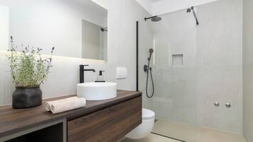 A modern bathroom with a wooden vanity, a white sink, a glass shower enclosure, and a potted plant.