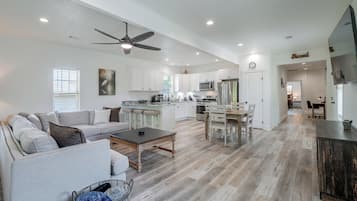 A spacious living area with a sofa, coffee table, and a dining table with chairs. A kitchen with modern appliances is visible in the background.