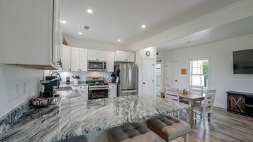 A modern kitchen with white cabinets, a marble island, and stainless steel appliances.
