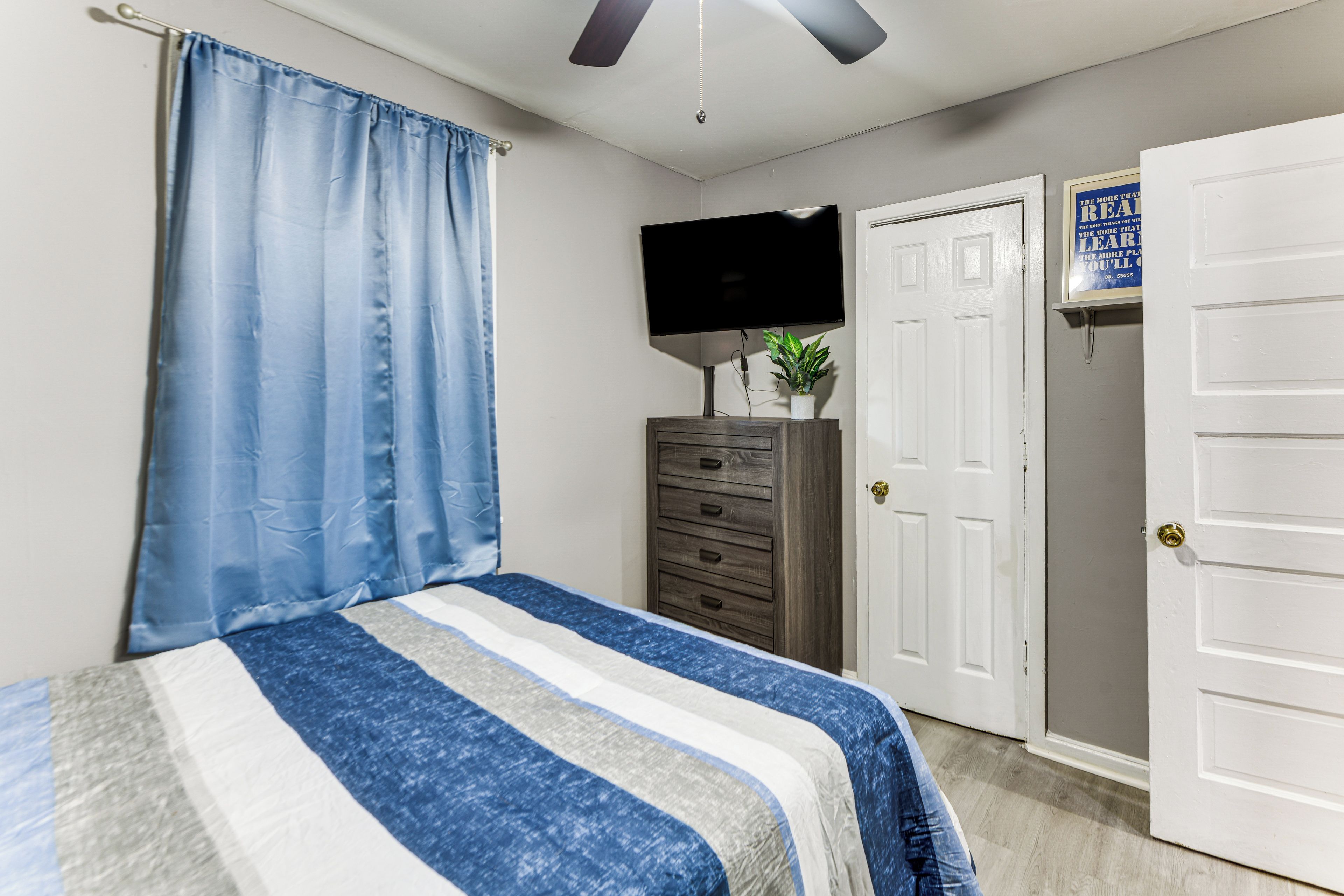 A bedroom with a bed, a dresser, a television, and a door.