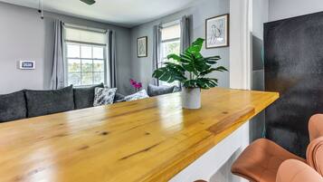 A modern living room with a wooden dining table, grey sofas, and a large potted plant.