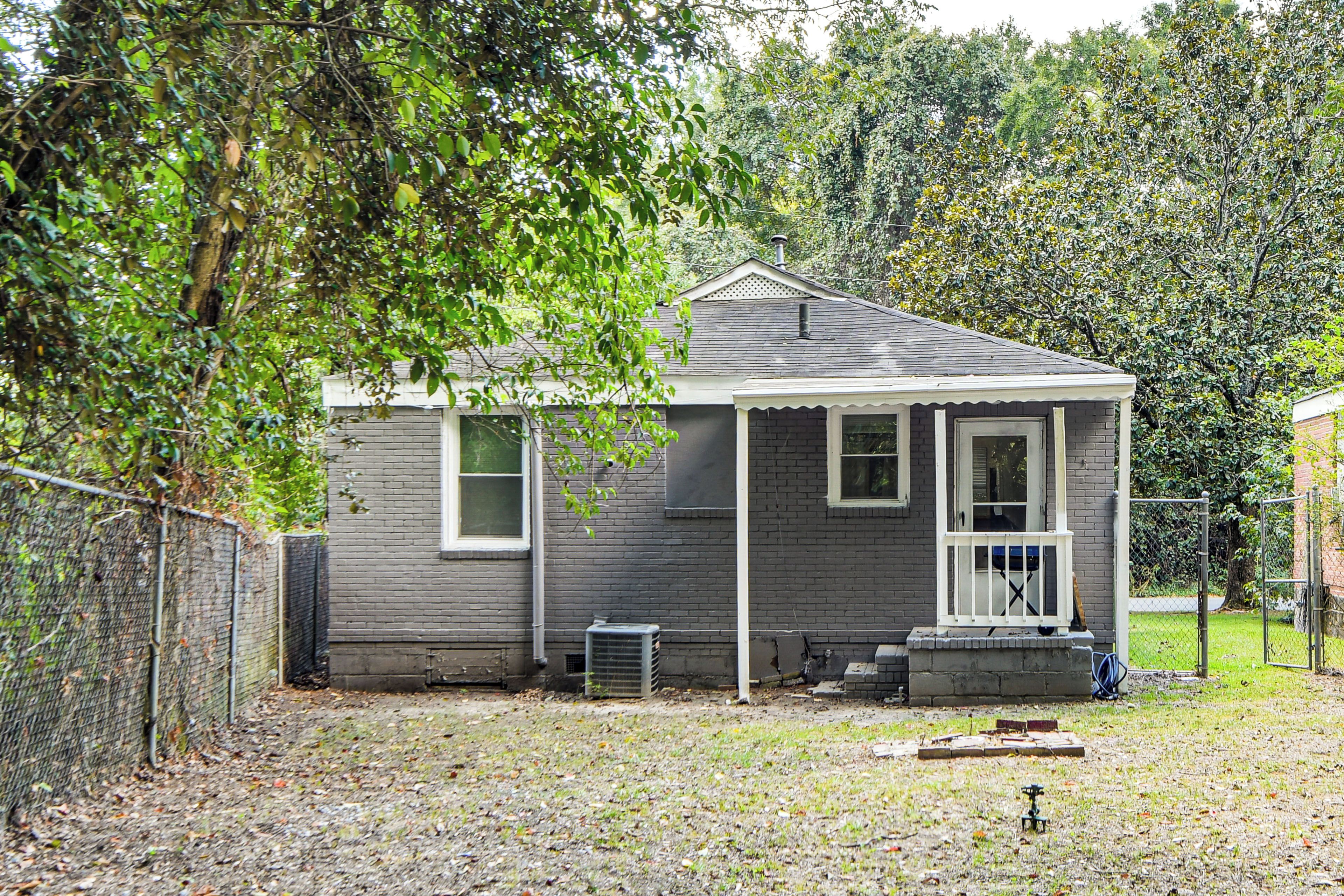 A small, single-story house with a porch, a fenced yard, and a chimney.