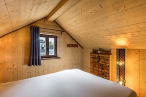 Une pièce avec un plafond en pente, un lit, une fenêtre avec des rideaux et une armoire en bois.