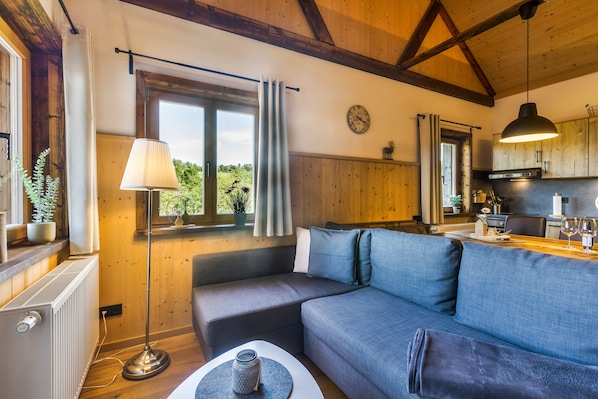 Un salon confortable avec un canapé, une lampe, une fenêtre avec des rideaux et une vue sur l’extérieur.