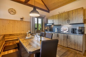 Un intérieur en bois comprenant une table à manger, des chaises, une horloge et un coin cuisine avec des placards et des appareils électroménagers.