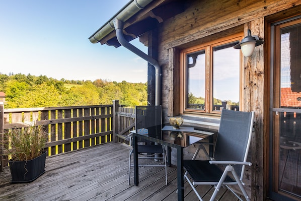 A wooden deck with a table and chairs, overlooking a forested area. - Chalet "Oberwald 2" with Private Terrace, Garden, Sauna, Wi-Fi, and Parking (Schotten)