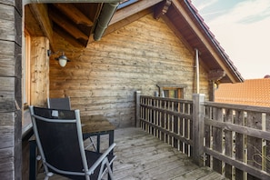 En træterrasse med et bord og stole, et gelænder og udsigt til et rødt tegltag.