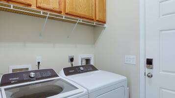 A laundry room with two front-loading washers, wooden cabinets above, and a white door.
