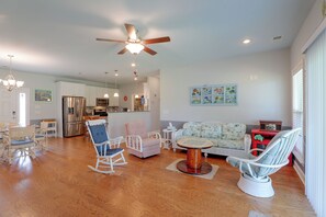 A spacious living room with a wooden floor, a ceiling fan, a dining area with wicker furniture, and a kitchen in the background. - Lake Marion Retreat Dock Days & Backyard Nights (Summerton)