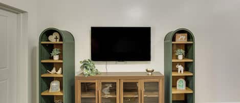 A room with a wooden cabinet, two green shelves, a flat-screen TV, and a small table.