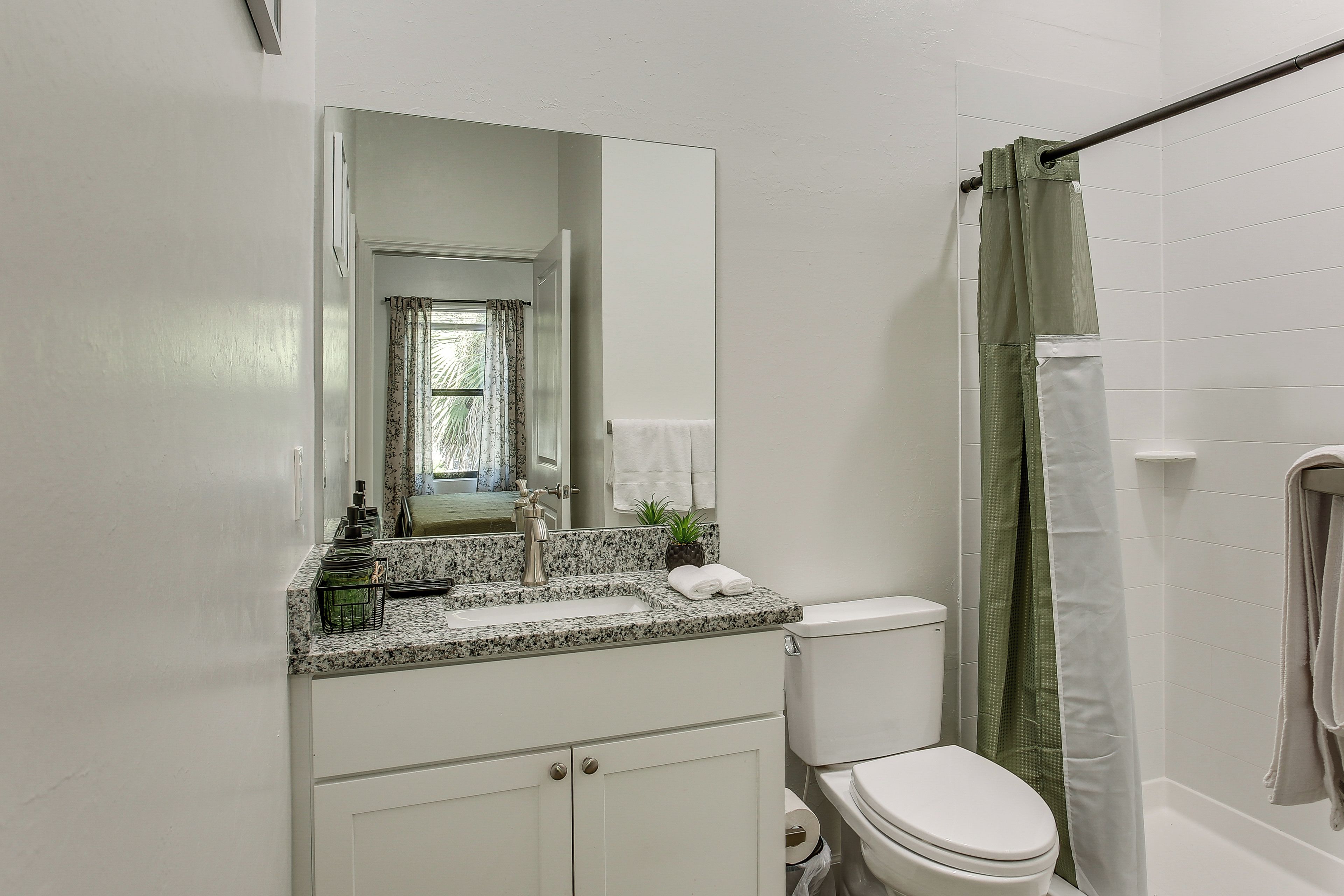 A bathroom with a white toilet, a sink with a granite countertop, a mirror, and a shower curtain.