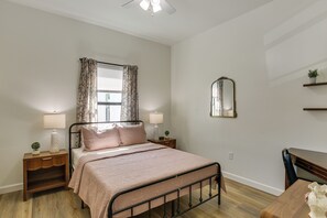 Un dormitorio con una cama, dos mesitas de noche, un tocador, un espejo, una ventana con cortinas y un aparador de madera.