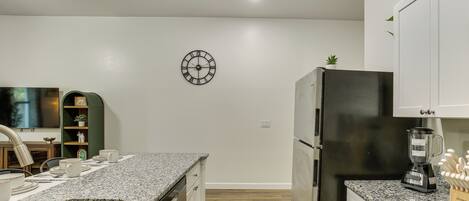 A kitchen with granite countertops, a stainless steel sink, a black refrigerator, and a wall-mounted clock.