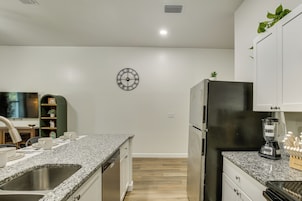 A kitchen with granite countertops, a stainless steel sink, a black refrigerator, and a wall-mounted clock.