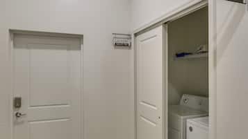 A laundry room with a washer and dryer, a sign indicating 'LAUNDRY WASH - DRY - FOLD', and a door with a key in the lock.