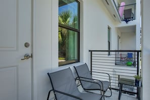 Un balcón con mesa y sillas, una ventana con vistas a palmeras y una puerta.