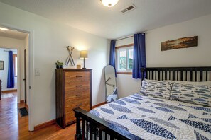 A bedroom with a wooden dresser, a bed with a patterned quilt, a window with curtains, and a painting on the wall. - Spacious Home w/ Deck & Mississippi River Views (Grafton)