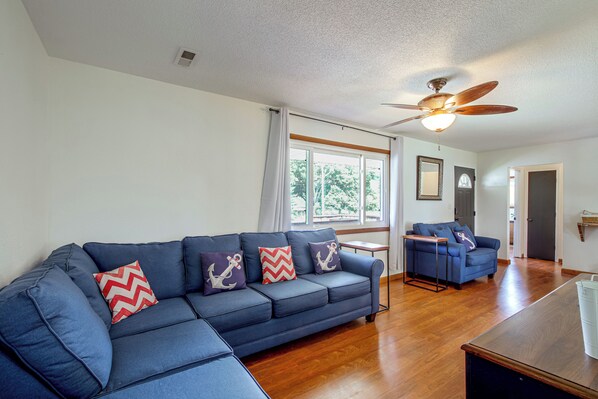 A living room with a blue sofa, wooden flooring, a ceiling fan, and a view through the windows. - Spacious Home w/ Deck & Mississippi River Views (Grafton)