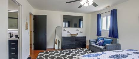 Un dormitorio con cama, cómoda, ventilador de techo, ventana con cortinas y espejo en la pared.