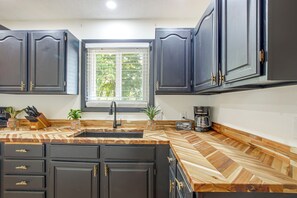 A kitchen with dark cabinets, a wooden herringbone countertop, a sink, and a window with blinds.