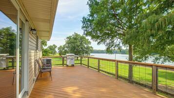 Une terrasse en bois avec un barbecue et des chaises, donnant sur un lac et une forêt.