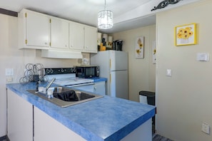 A compact kitchen with white cabinets, a blue countertop, a stainless steel sink, a black microwave, and a white refrigerator. - Fort Stockton Home, Your Big Bend Basecamp (Fort Stockton)