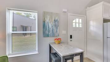A room with a window, a door, a table with a bowl of snacks, and a painting on the wall.