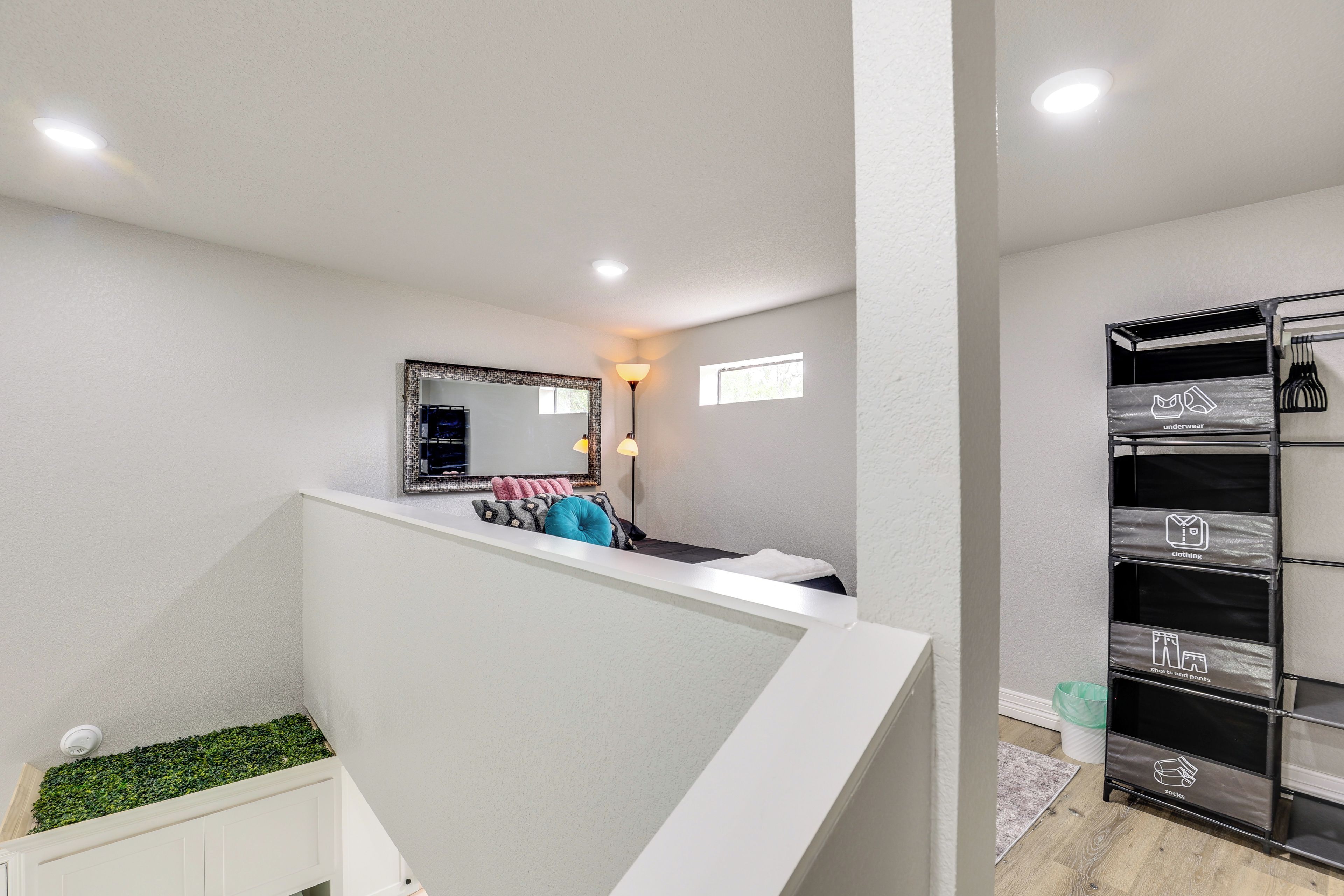 A modern interior with a white staircase, a mirror, a small window, and a clothing storage unit.